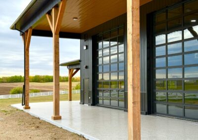 Up-close exterior view of full-view glass garage doors and heavy timber porch framing on a modern country shop build in Alberta.