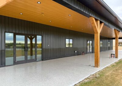 Covered side porch of a premium commercial acreage building featuring warm wood-finished ceilings, recessed lighting, and timber support posts by Vantage Builders.